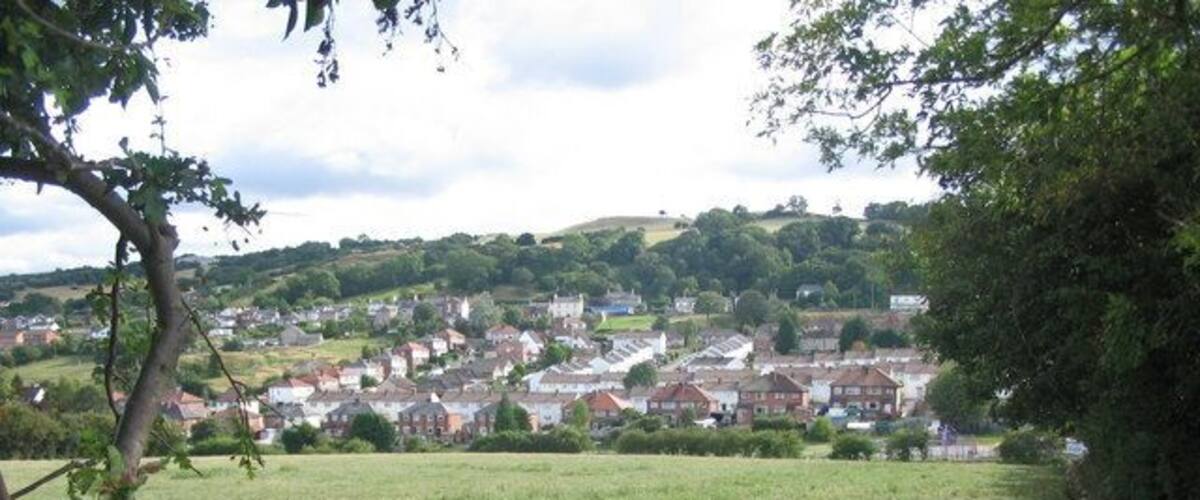 A rural landscape with a field, trees, and a village in the distance.
