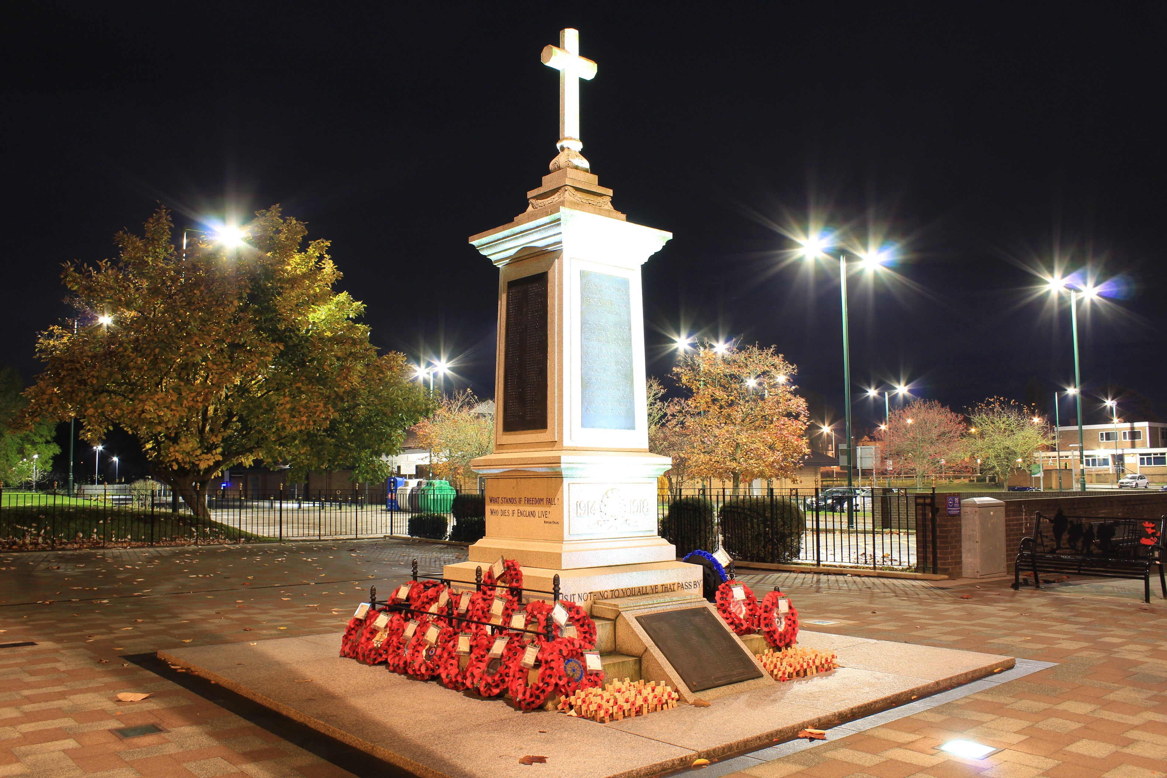 A monument with a cross, surrounded by red poppy wreaths, at night.