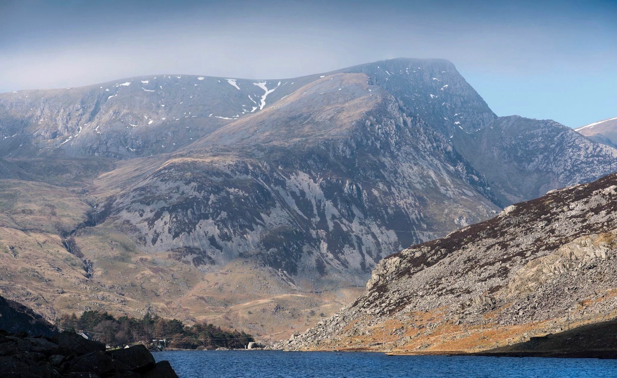 A mountainous landscape with a lake in the foreground and a prominent peak in the background.