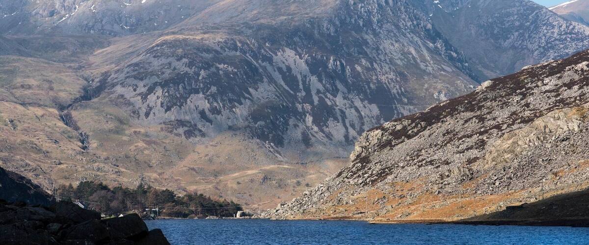 A mountainous landscape with a lake in the foreground and a prominent peak in the background.