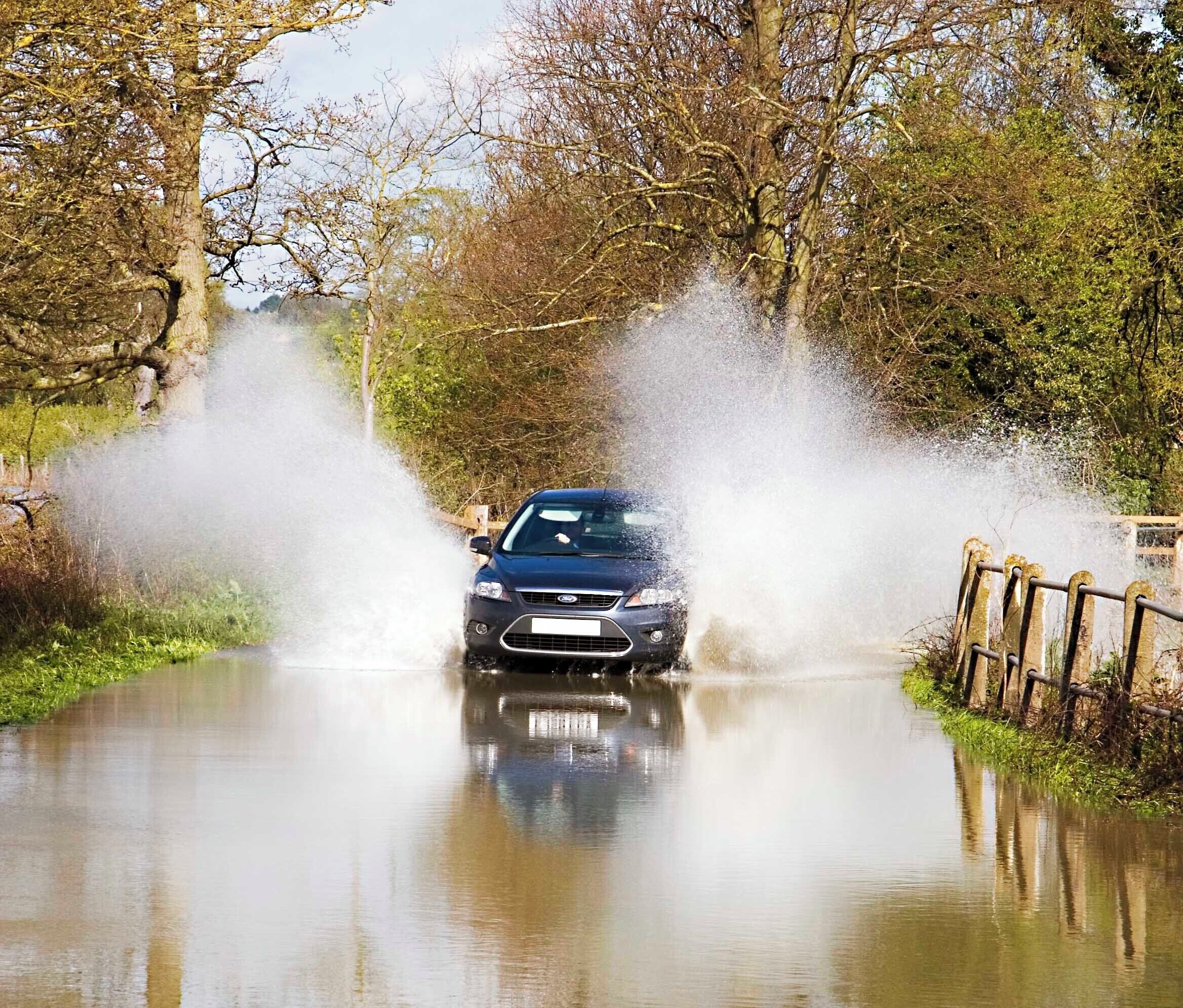 A car driving through a flooded road with water spraying up around it.