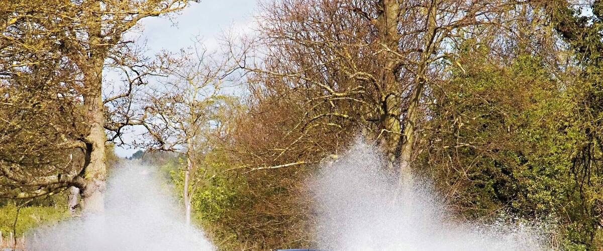 A car driving through a flooded road with water spraying up around it.