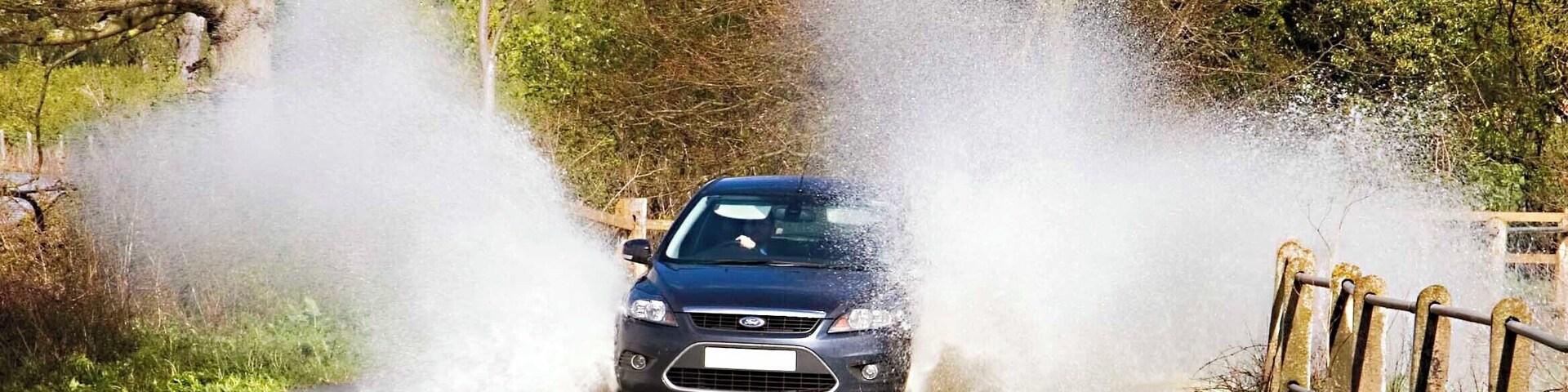 A car driving through a flooded road with water spraying up around it.