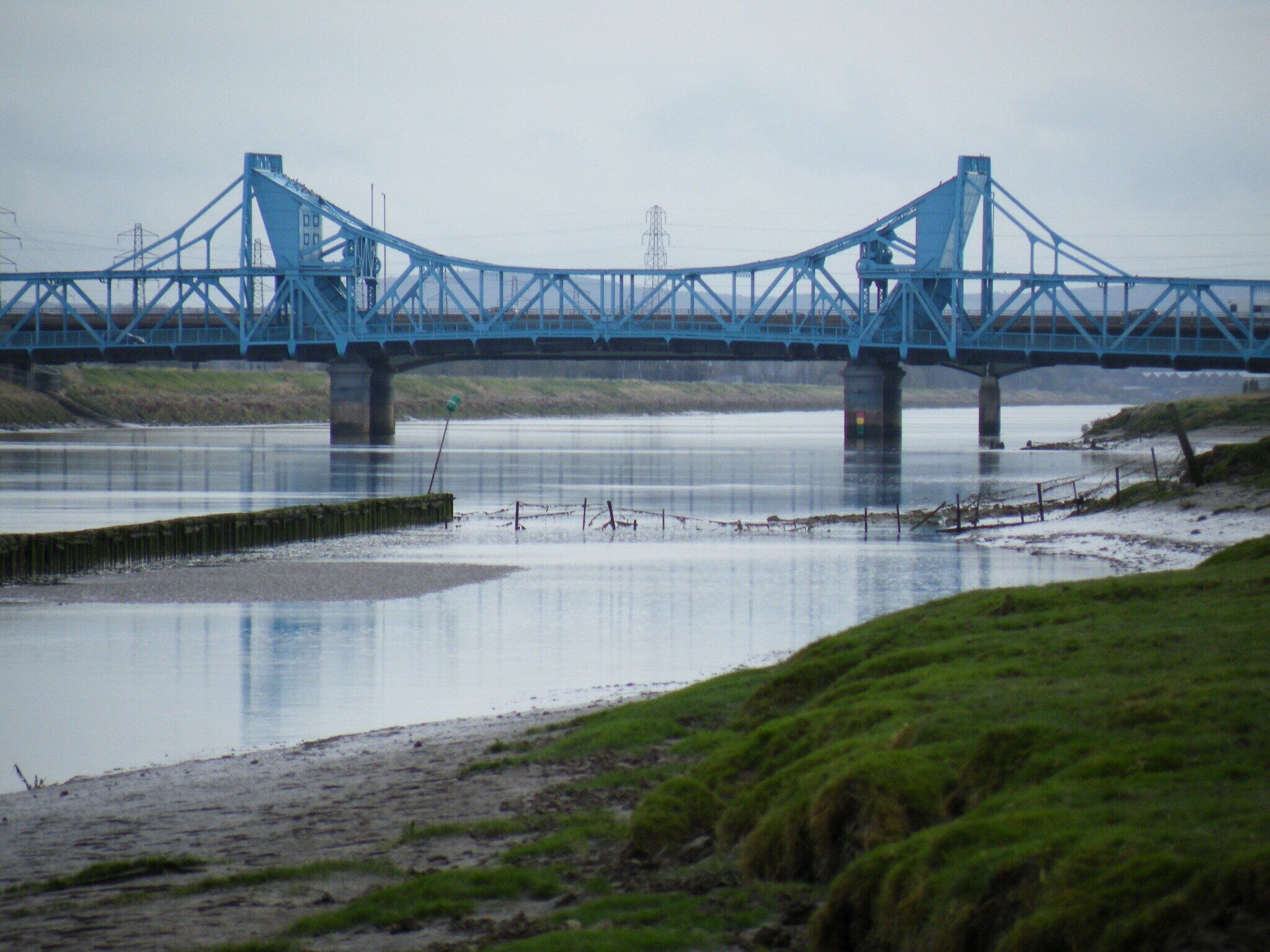 A blue bridge over a river with grassy banks.