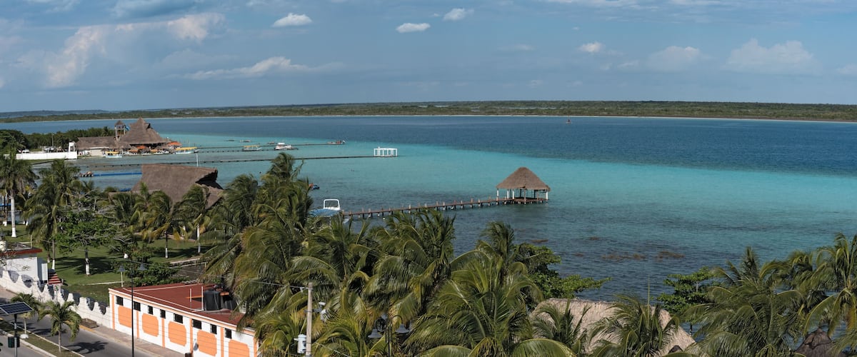 A tropical beach with clear turquoise waters, a pier, and palm trees.