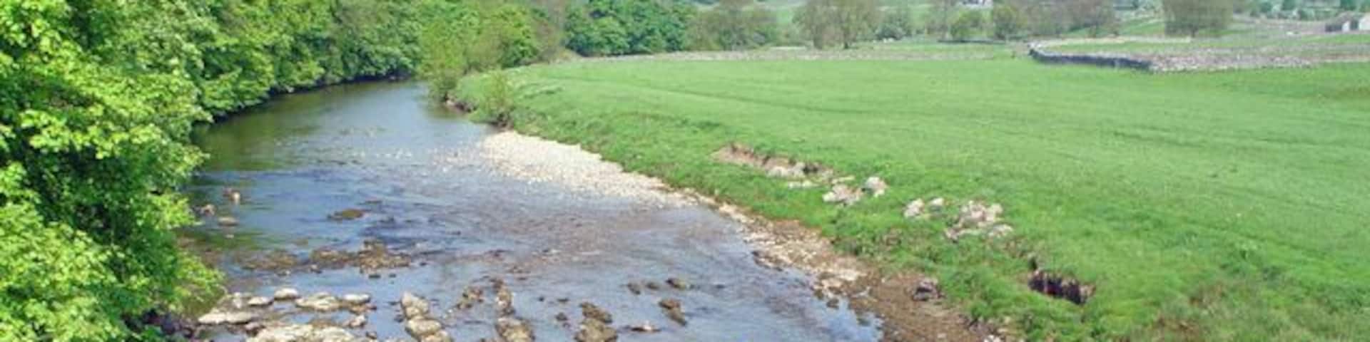 River Wharfe from the Grassington Bridge, Grassington, North Yorkshire. Looking northwest. The eastern bank of the river Wharfe carries the Dales Way long distance footpath at this point. On the skyline is Grass Wood.