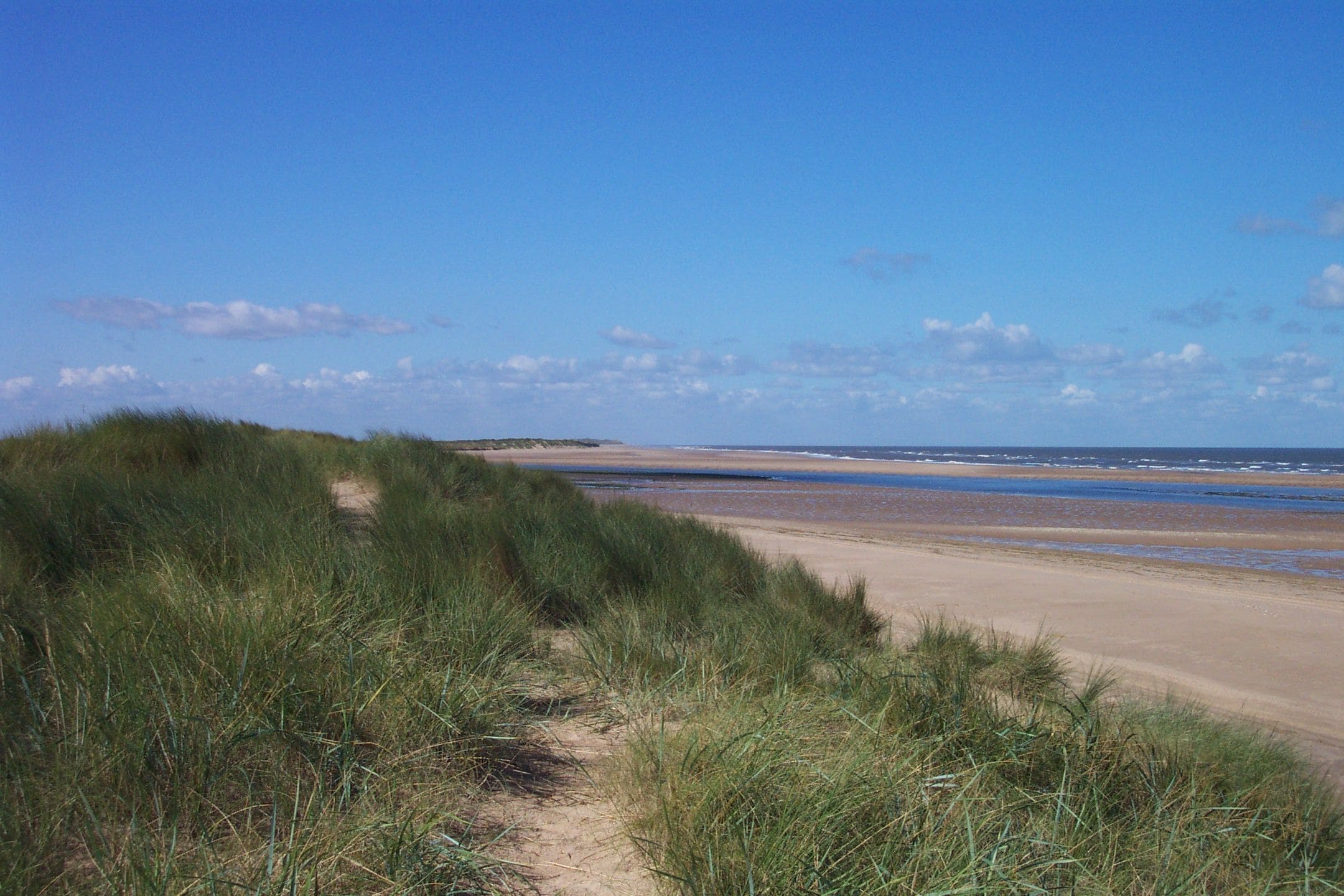 The coast near Burnham Overy Staithe, taken from the crest of the dunes at the end of the footpath from Staithe to beach. Beyond the dunes can be seen the entrance to the River Burn, which gives boat access to the Staithe. Beyond that is Scolt Head Island, a nature reserve accessible only by boat. For more information see the Wikipedia article Burnham Overy.