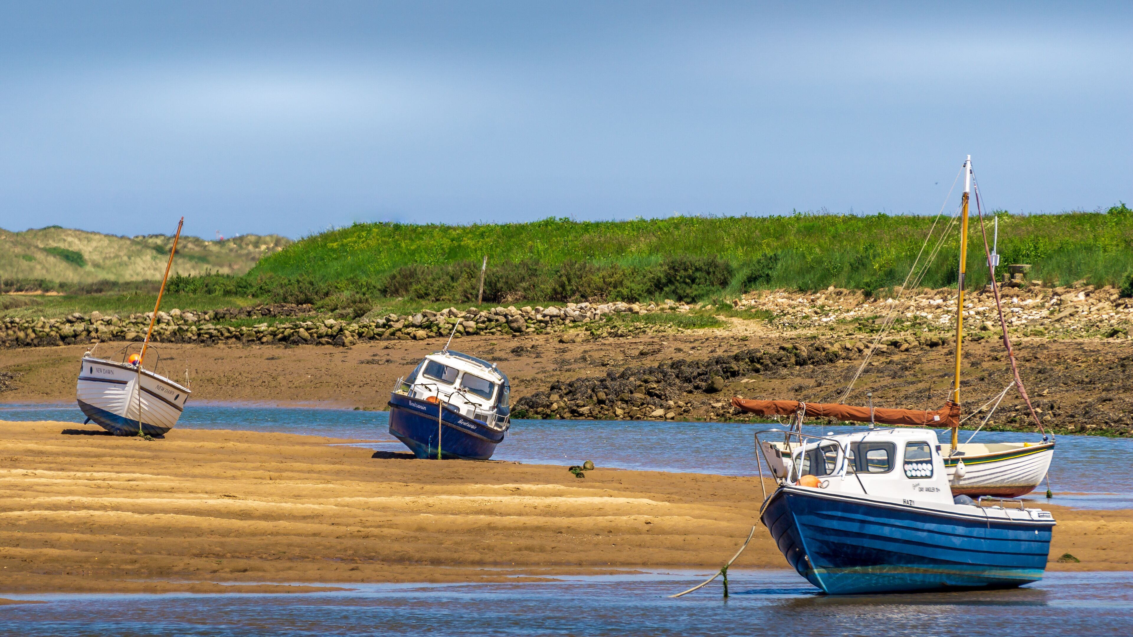 Three boats on a sandy beach with a rocky shoreline and green vegetation in the background.