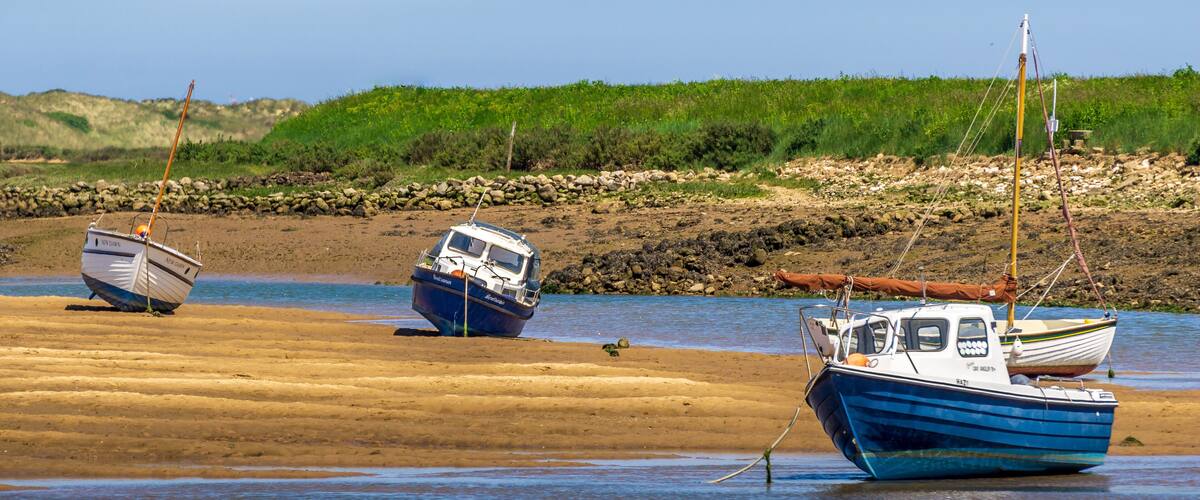 Three boats on a sandy beach with a rocky shoreline and green vegetation in the background.
