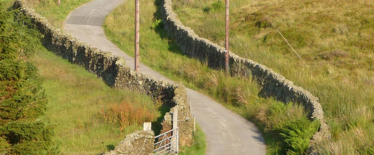A winding country road with stone walls on one side and a grassy field on the other.