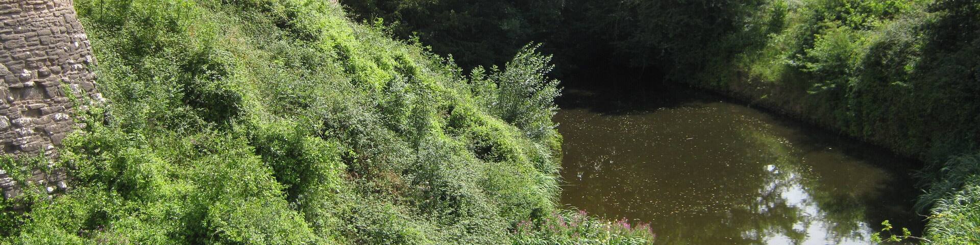 A historic stone tower and lush greenery beside a calm river.