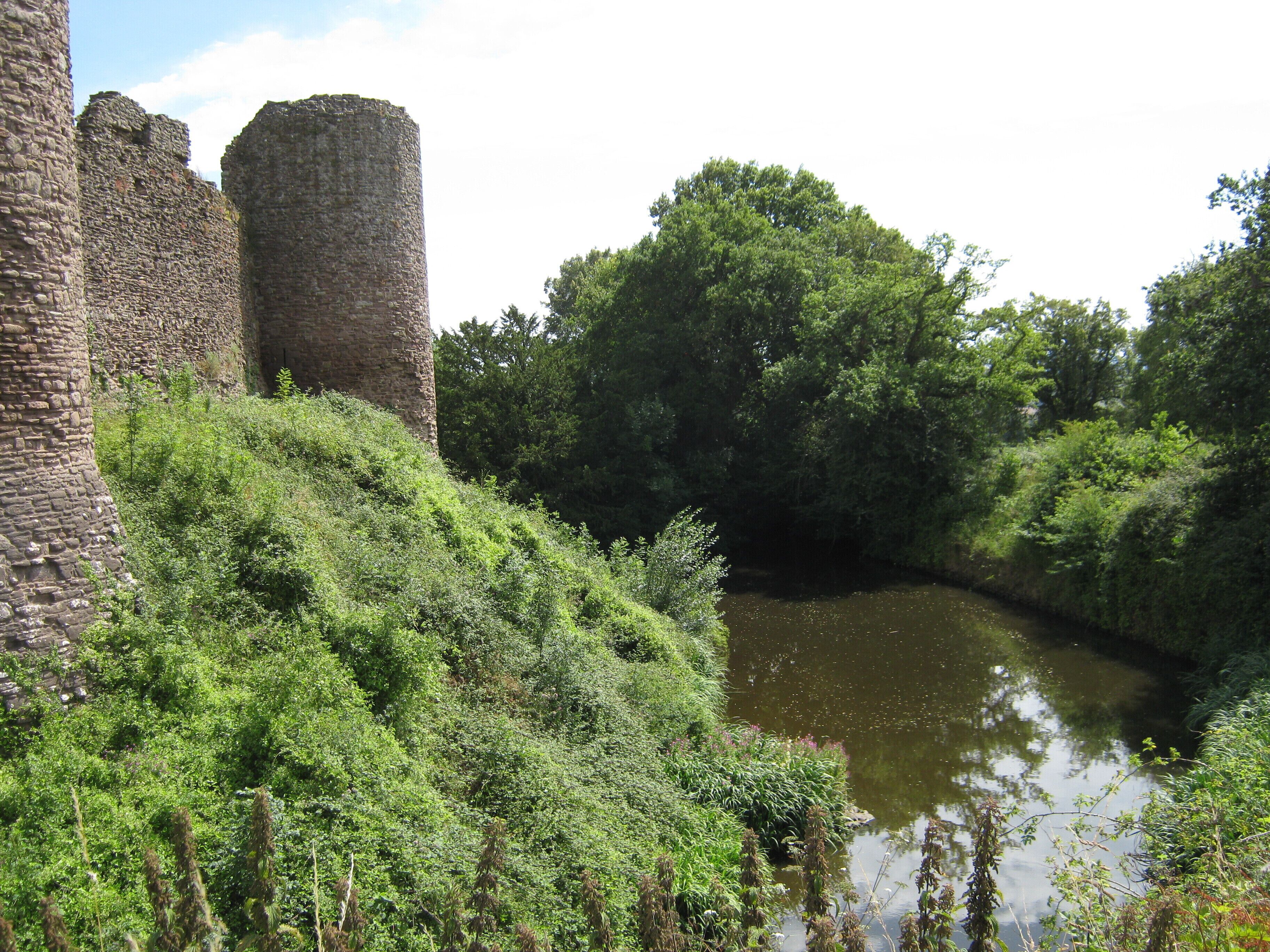 A historic stone tower and lush greenery beside a calm river.