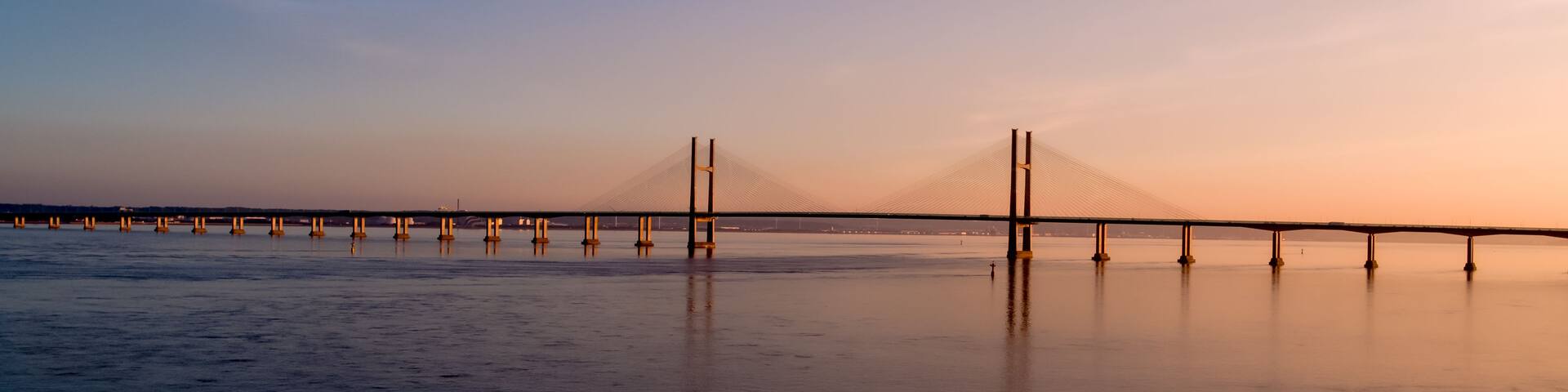 A suspension bridge over a calm body of water during sunset.