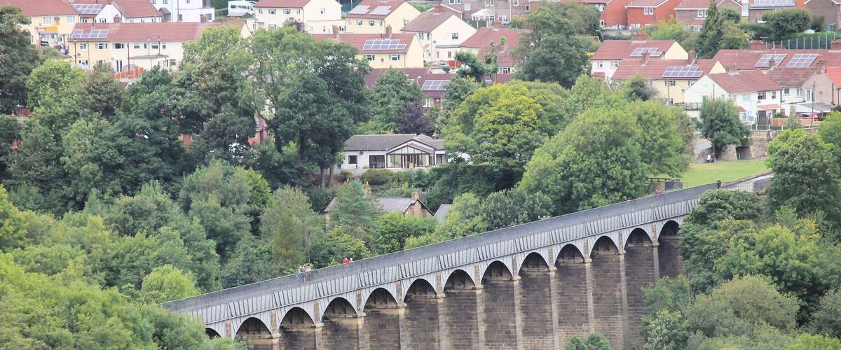A viaduct over a river with houses in the background.