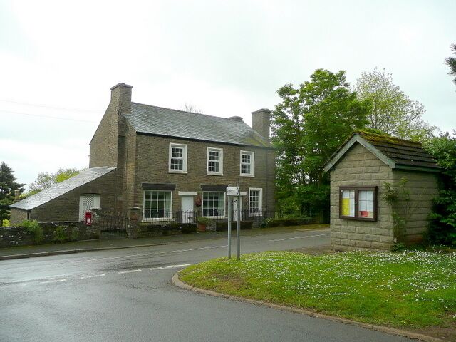 A stone building with a sloped roof, a small adjacent structure, and a road leading to it.