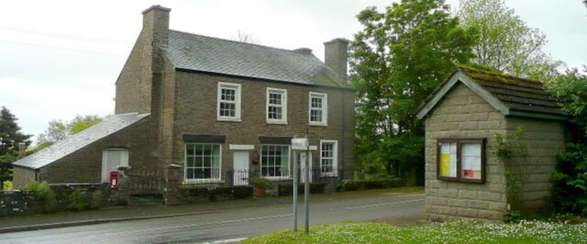 A stone building with a sloped roof, a small adjacent structure, and a road leading to it.