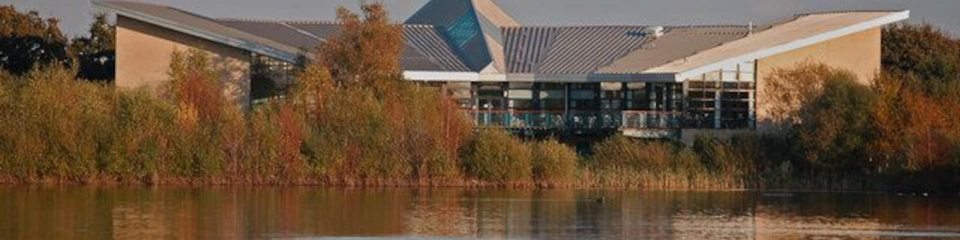 Um edifício moderno com fachada de vidro triangular e um espelho d'água refletivo na frente.