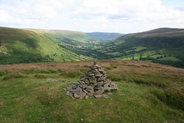 A stone cairn on a grassy hill with a valley in the background.