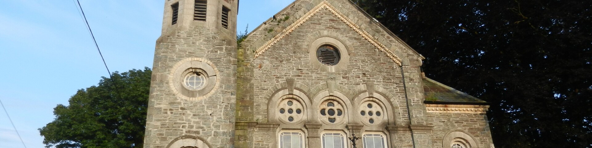 Igreja de pedra com uma torre alta e telhado pontiagudo.