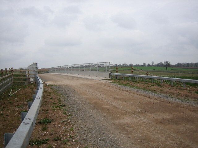 A dirt road leading to a fenced area with a bridge.