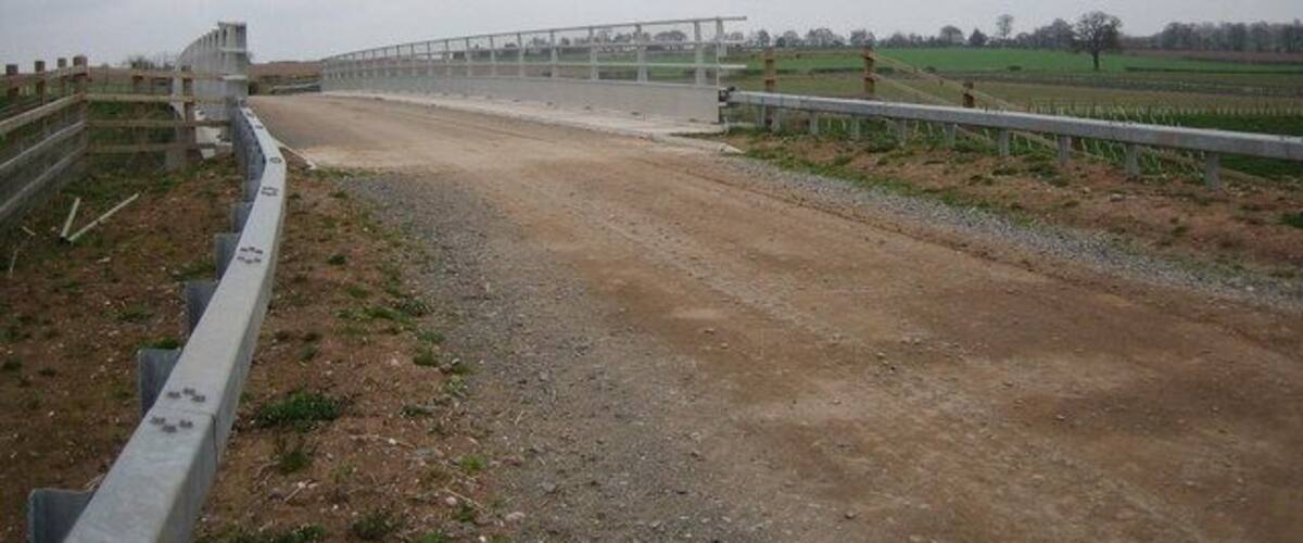 A dirt road leading to a fenced area with a bridge.