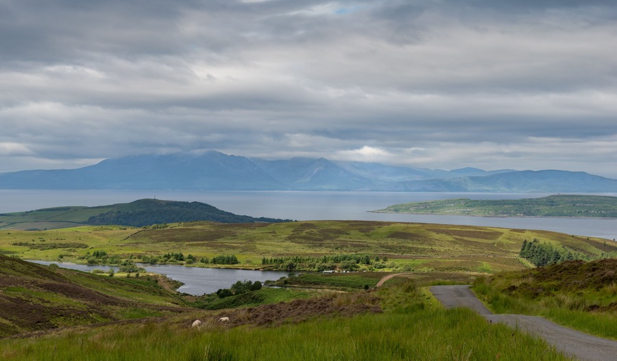 A scenic landscape with rolling hills, a lake, and distant mountains under a cloudy sky.