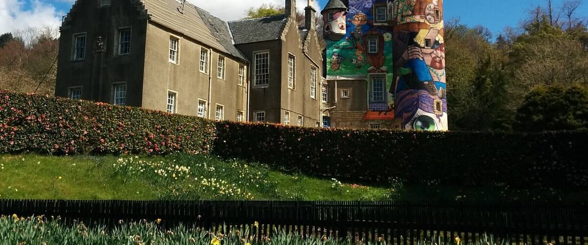 A castle with colorful murals, a large garden, and a clear blue sky.