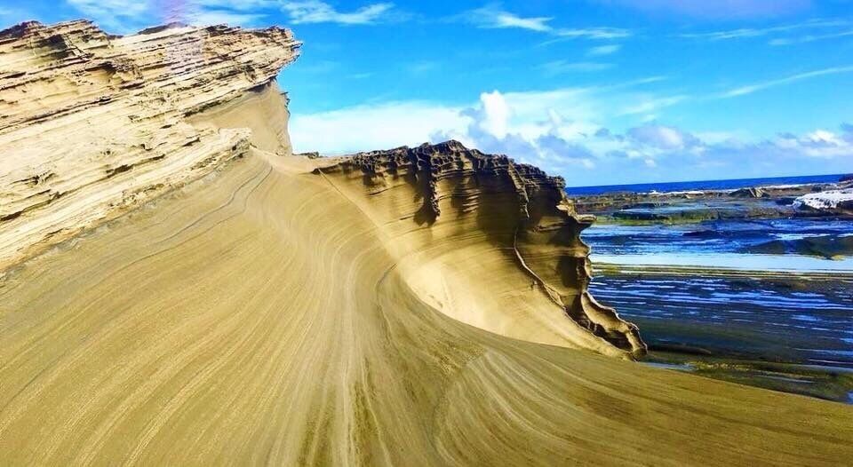 A large sand dune with a steep cliff on the left and a curved shoreline.
