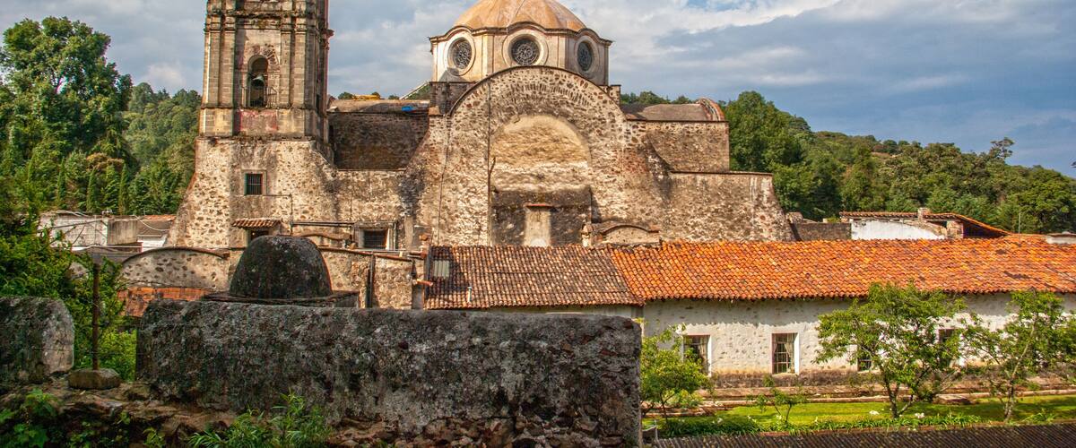 An old church with a bell tower and dome, surrounded by greenery and trees.