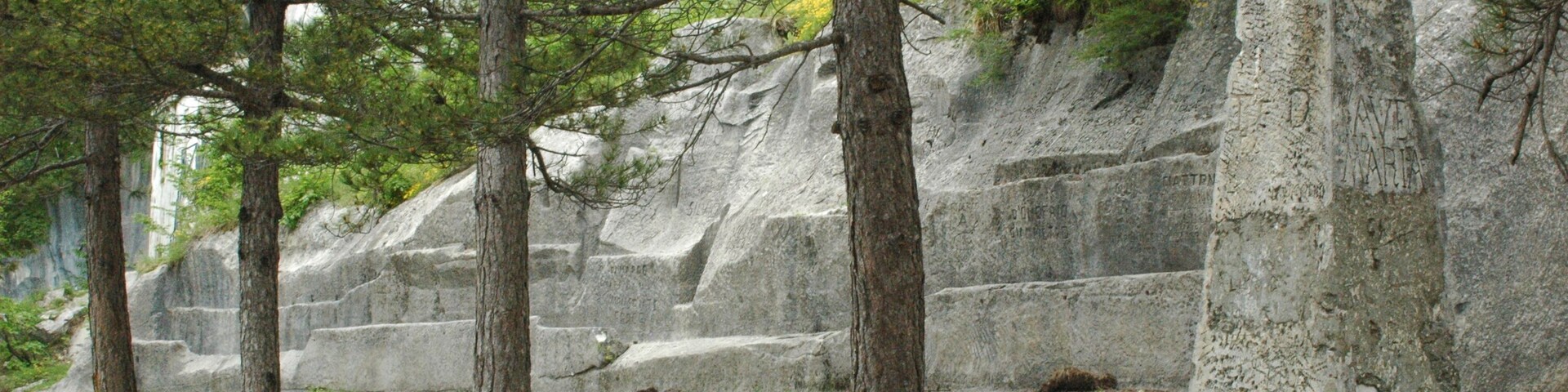 Un monumento de piedra con una parte superior esférica, rodeado de árboles y una ladera rocosa.