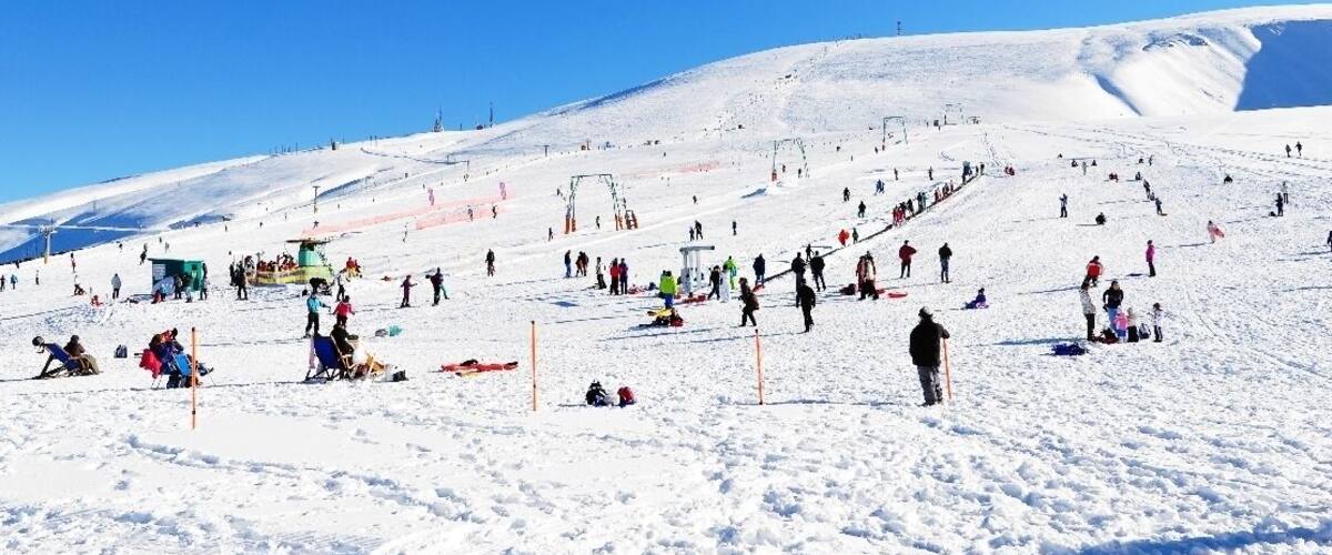 A snowy ski slope with skiers and snowboarders, a ski lift, and a clear blue sky.
