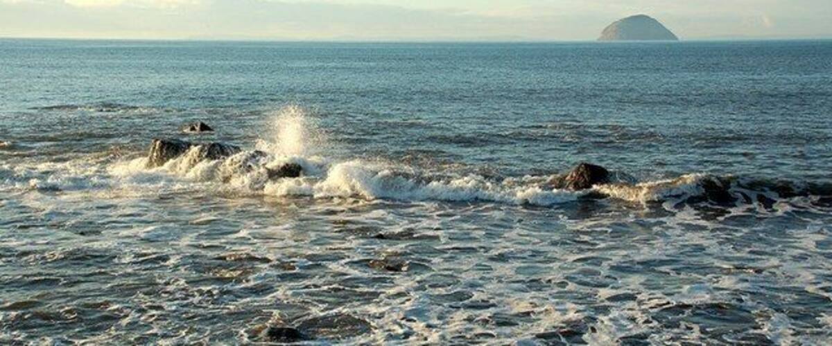 A coastal scene with waves crashing onto rocks and a distant island.