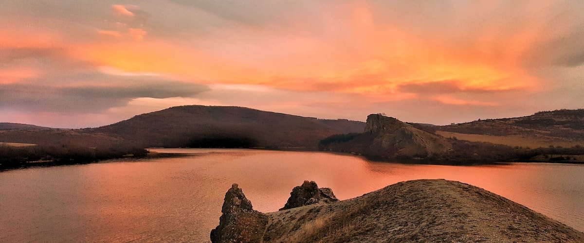 A sunset over a lake with rocky outcrops and hills in the background.