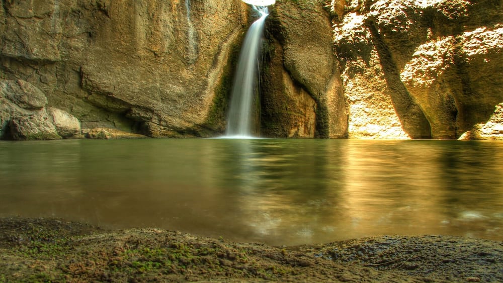 Ein Wasserfall stürzt in ein ruhiges Becken, umgeben von felsigen Klippen.