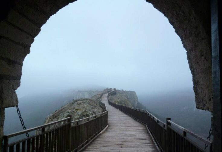 A foggy coastal walkway with a wooden deck and stone walls.