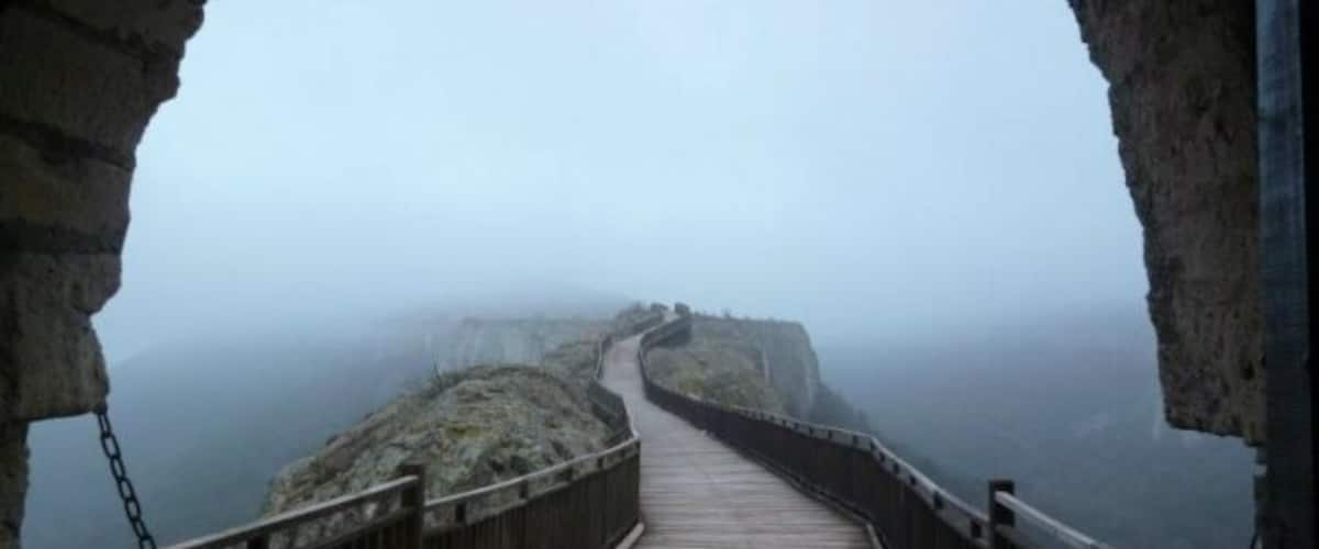 A foggy coastal walkway with a wooden deck and stone walls.