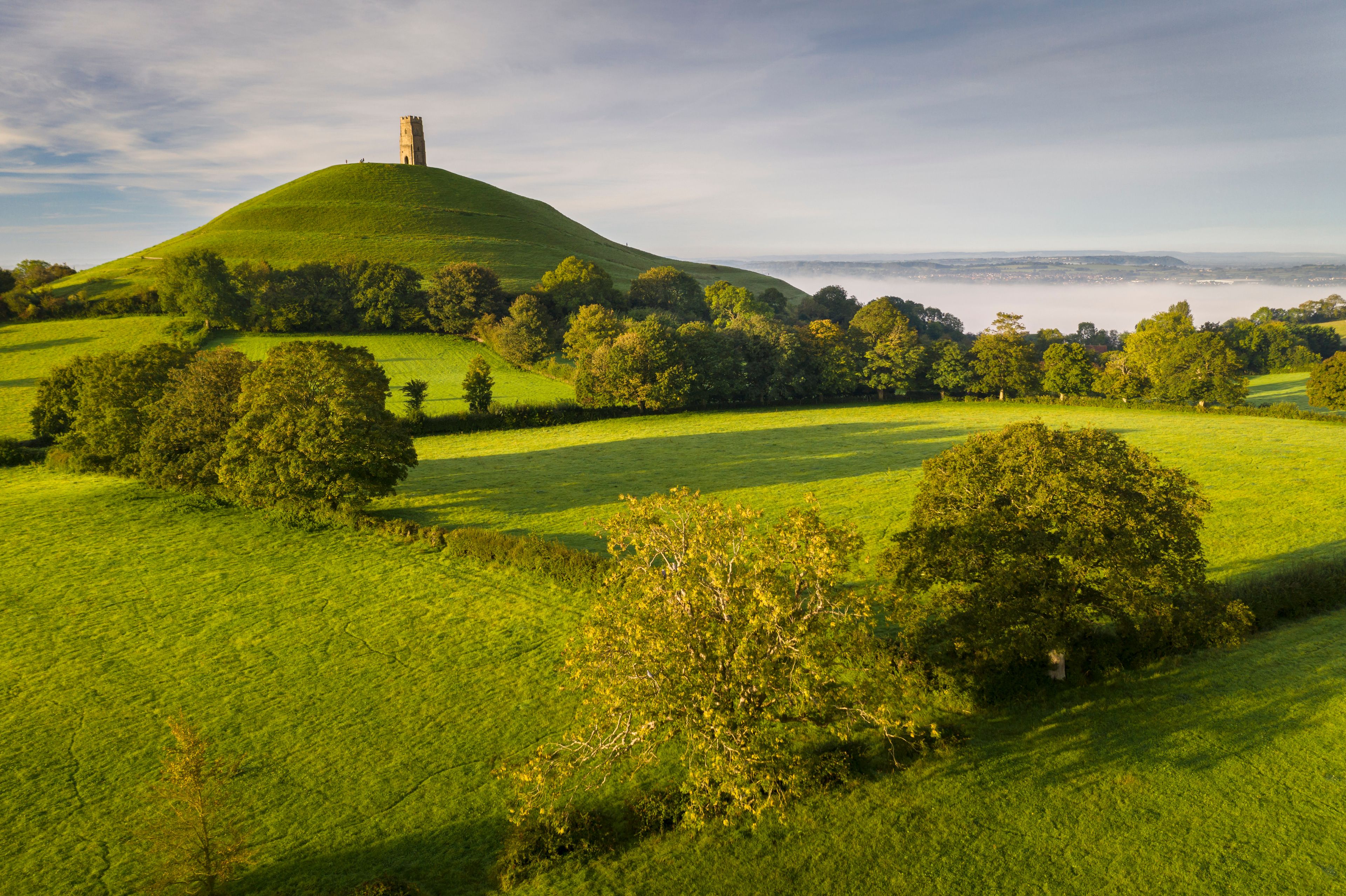 A green hill with a tower on top, surrounded by trees and fields.