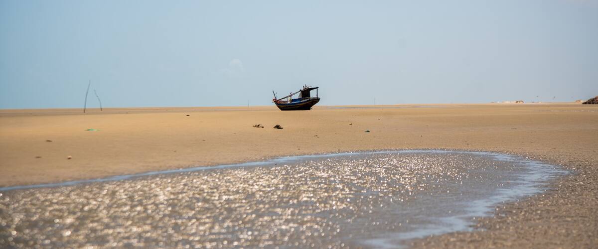 A boat on a sandy beach with a clear sky.