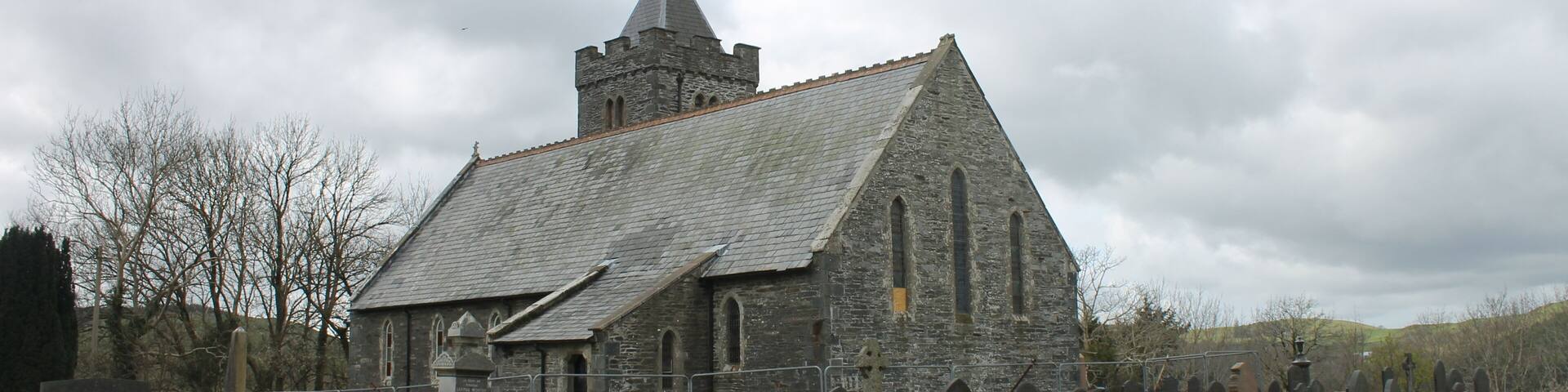 A stone church with a tower and a graveyard with numerous headstones.