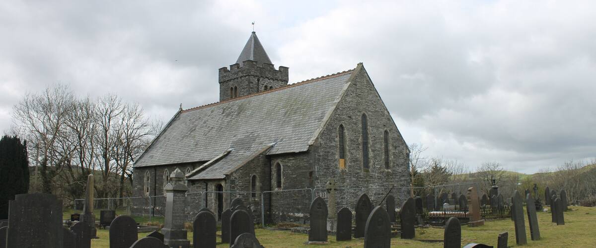 A stone church with a tower and a graveyard with numerous headstones.