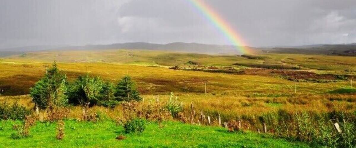 A rainbow over a grassy landscape with rolling hills in the background.