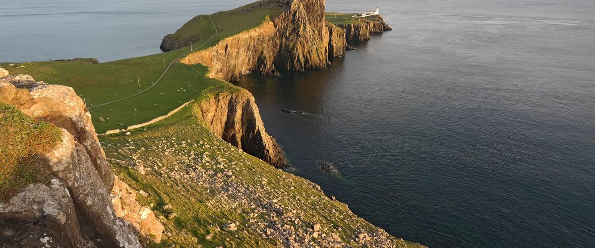 A coastal landscape with a prominent cliff, a lighthouse, and a grassy path.