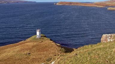 A lighthouse on a grassy cliff overlooking a large body of water.