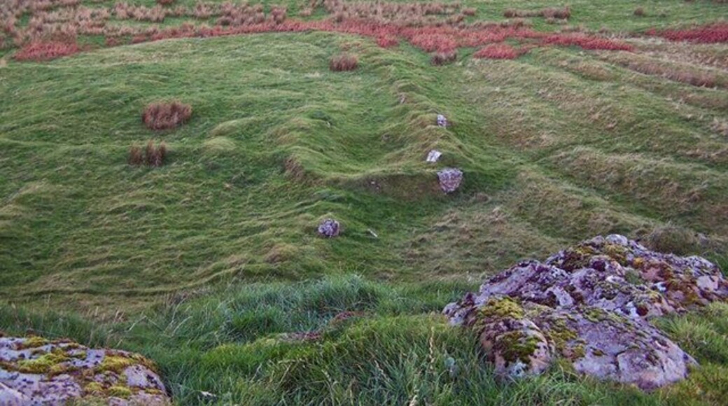 Ruin below Dun Chaich There is much evidence of lazybeds and ruined walls and buildings in this area. Here, looking down from the scant remains of Dun Chaich, the outline of a building and wall shows as humps in the grass. They may well have been built using stone robbed from the dun.