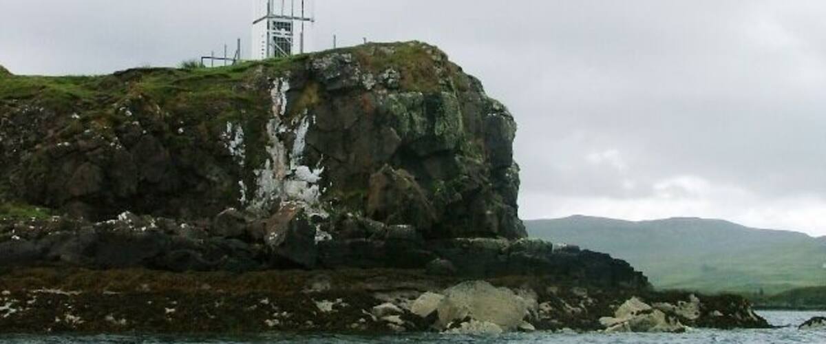 A rocky island with a lighthouse and a tower on top.