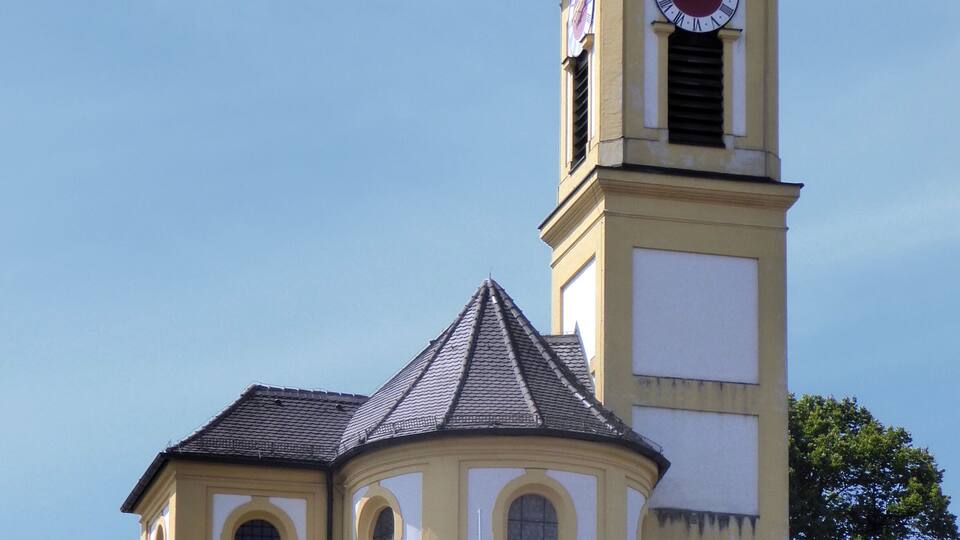 A yellow church with a clock tower and a weather vane.