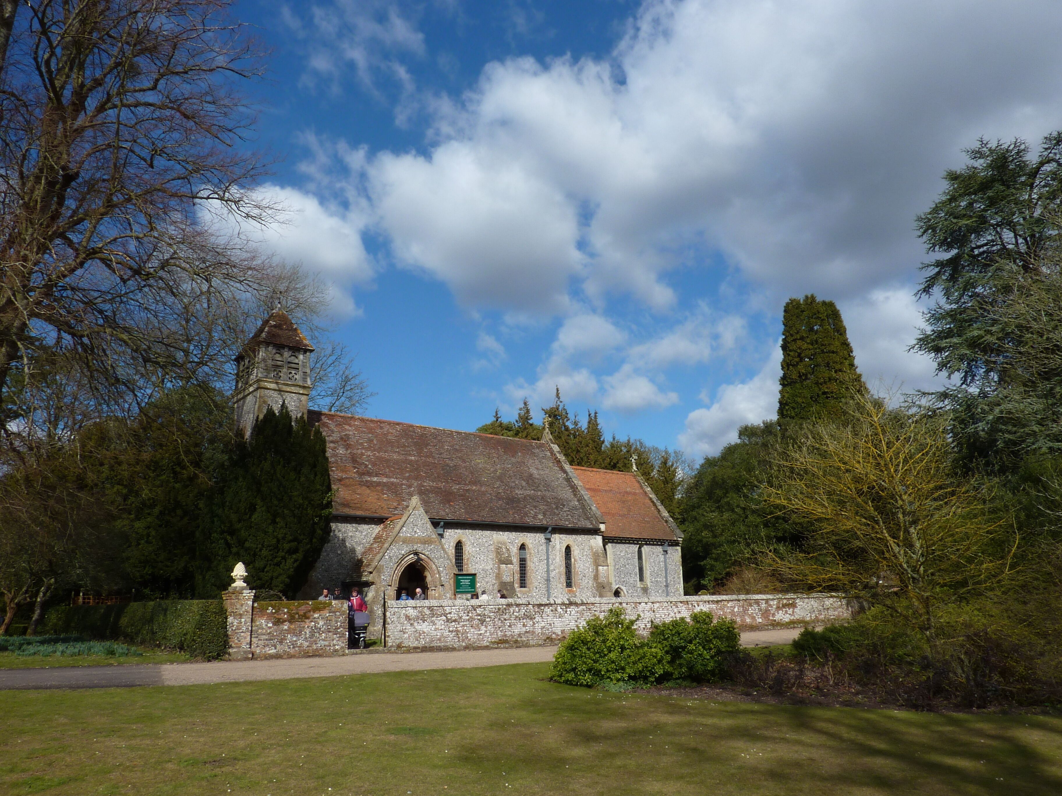 A historic stone church with a bell tower, surrounded by trees and a well-maintained lawn.