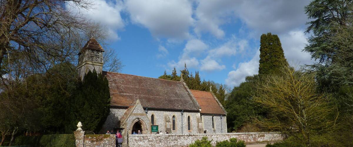 A historic stone church with a bell tower, surrounded by trees and a well-maintained lawn.