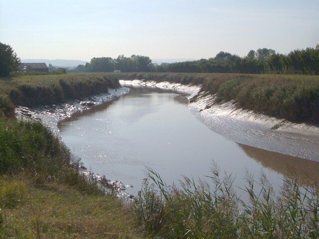 A river meandering through a rural landscape with grassy banks and distant trees.