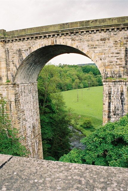 An old stone bridge with a green landscape and trees in the background.